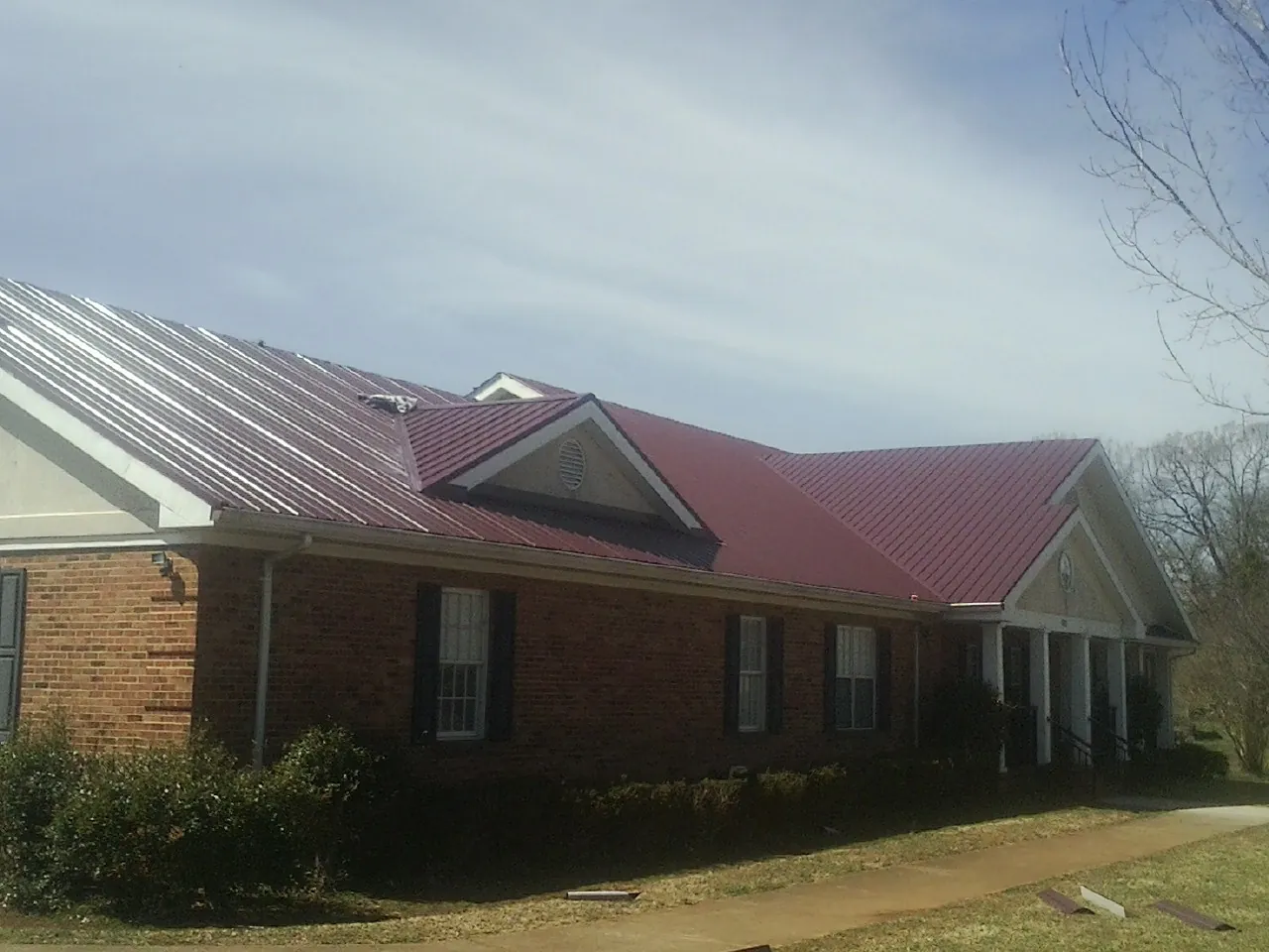Red metal roof with gabled entries on a long brick building, from a Hail Damage Roof Repair job in Union Springs