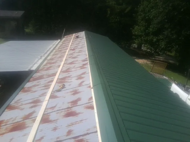 Old rusted panels beside newly installed green metal roofing — Wind Damage Roof Repair by Roofing Brothers in Union Springs
