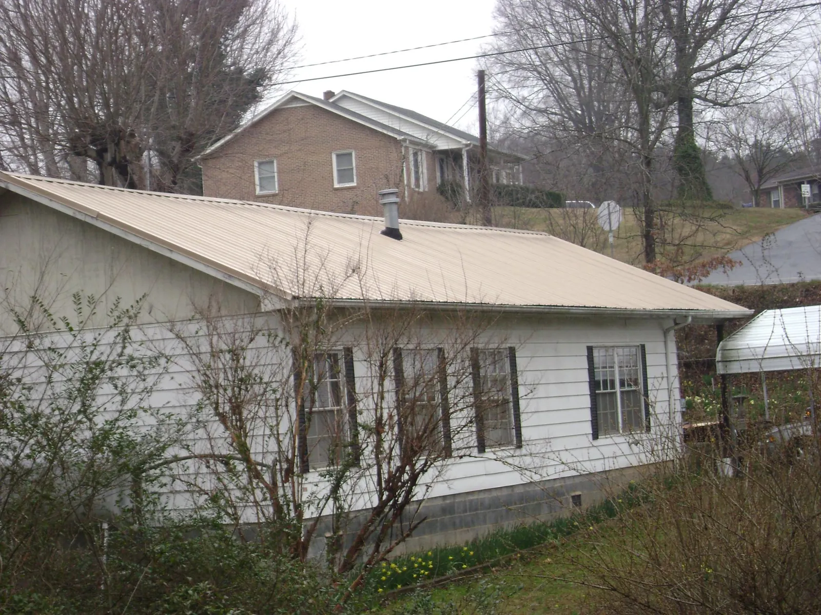 Tan metal roof on a white sided house set into a hillside — Commercial Roofing by Roofing Brothers in Union Springs