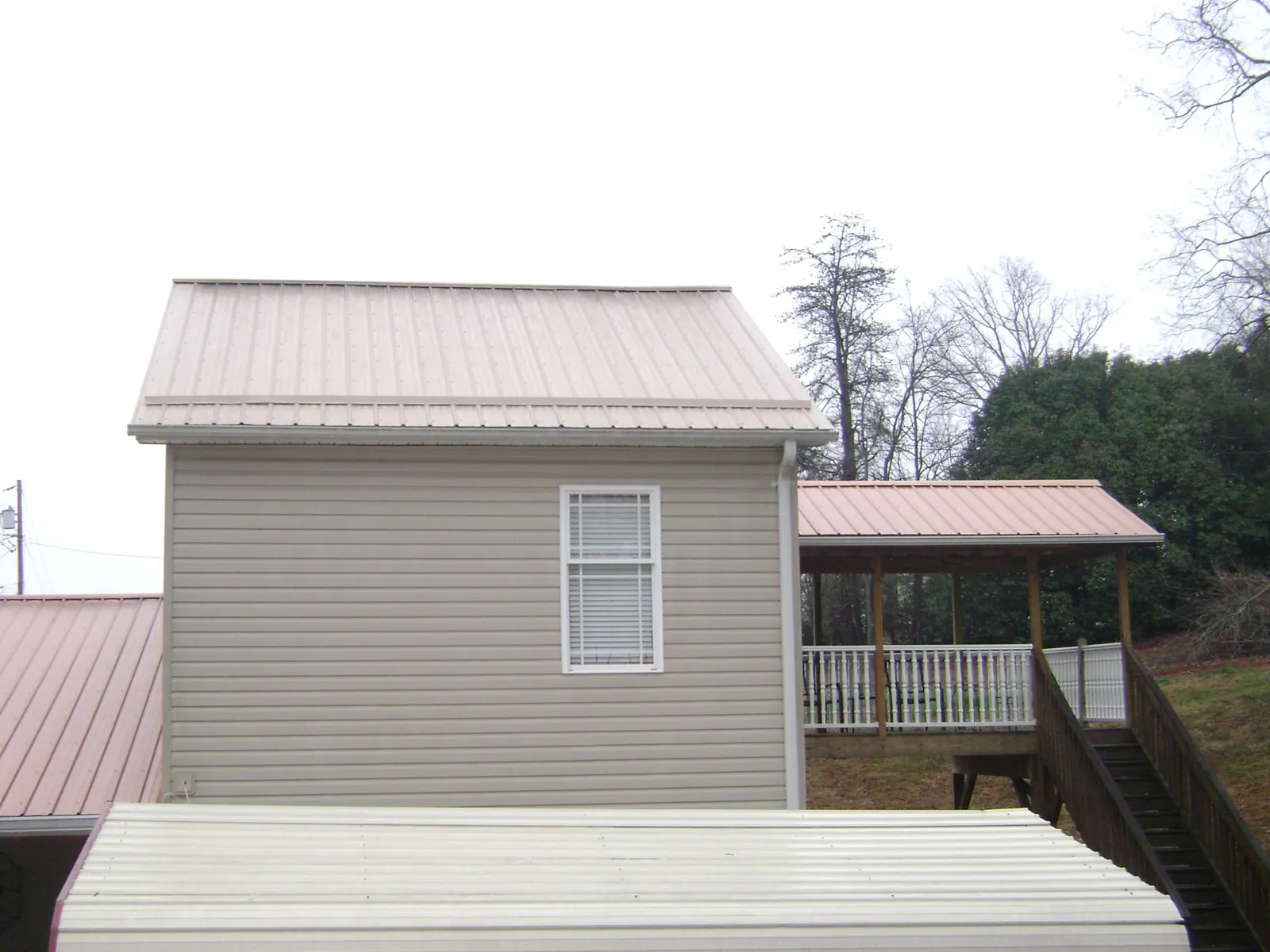 Tan metal roofs on a two story addition and attached porch, from a Roof Replacement job in Union Springs